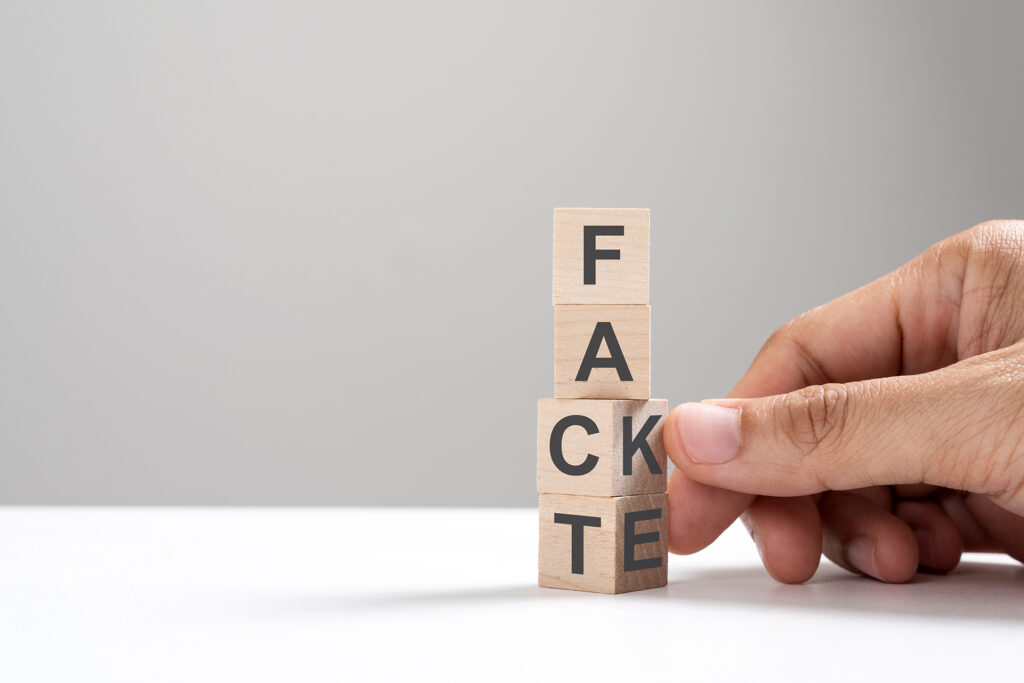 A hand is holding a wooden block with the word fake on it.