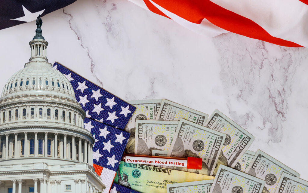 A pile of money and an American flag in front of the Capitol building.
