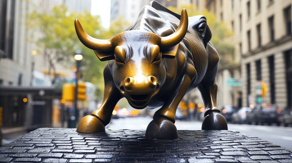 Bronze Charging Bull statue stands on a cobblestone pedestal in a city street, surrounded by tall buildings.